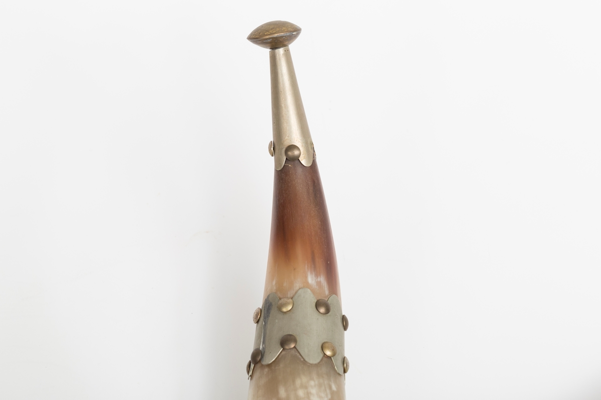 Knaggrekke antagelig håndlaget av kuhorn. 4 horn/kangger. Montert med "dekorative" beslag som er spikret og dekornaglet på hornene. Kledd med cordfløyelstoff på midtparti. To øyeskruer på toppen for feste til vegg.