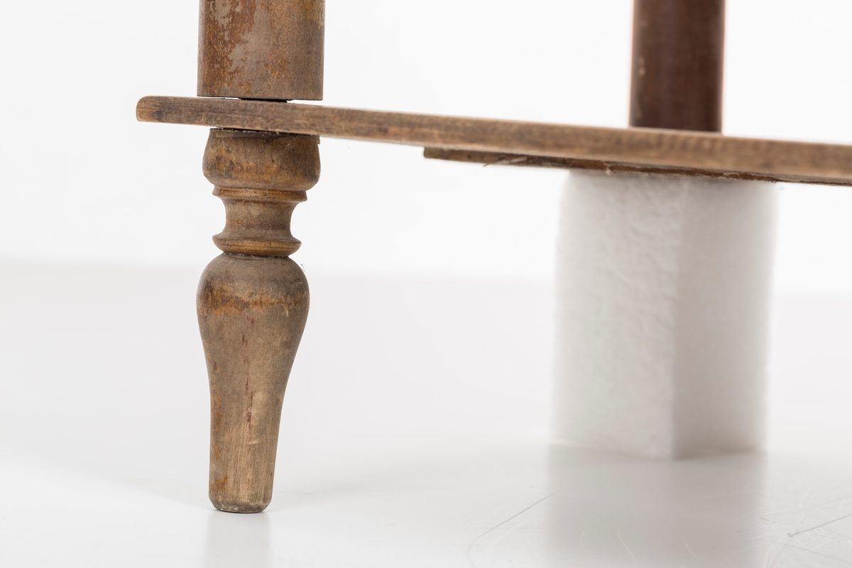 Hylle med 4 hyller. Dreide stolper mellom hyllene. Mangler ett bein. Sprosser øverst. Lakkert i mørk brunt.