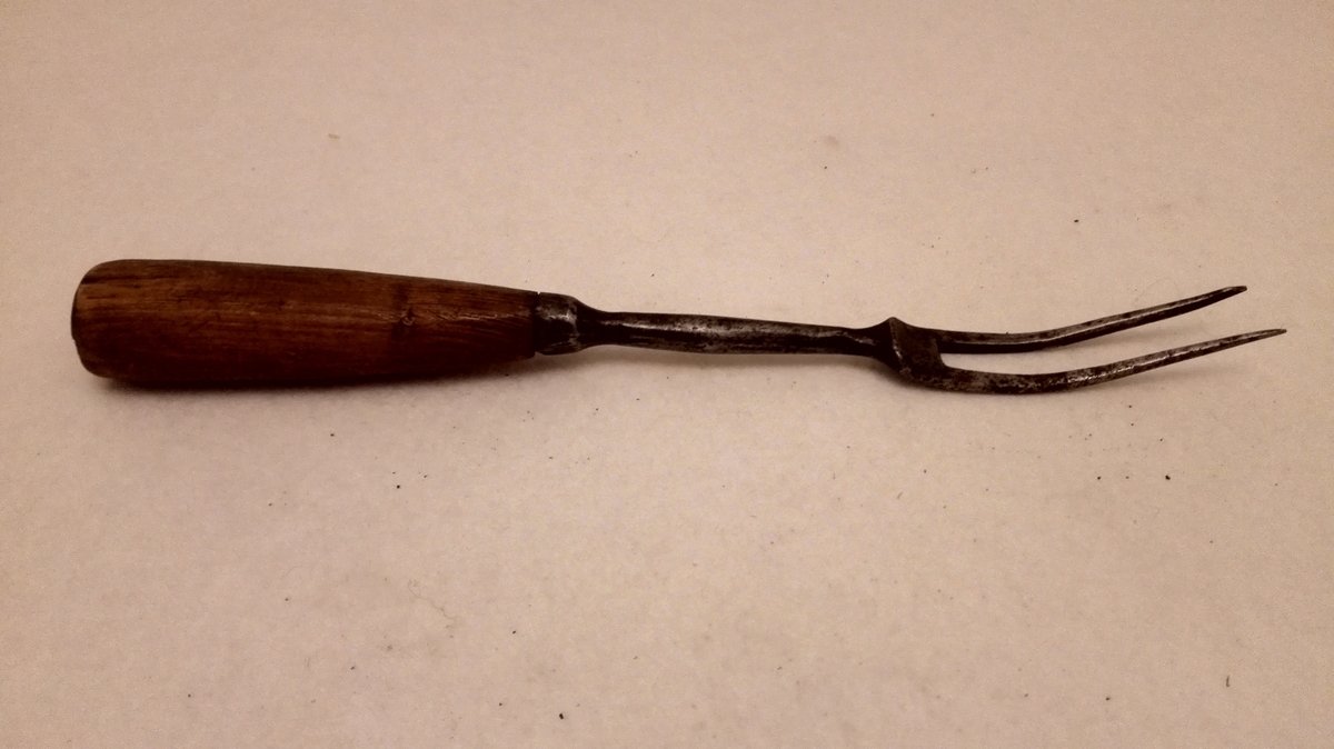 Form: Rundt skaft.
1 gaffel.

2 tindet gaffel av staal. Har 6 cm lang legg av staal og 6.7 cm langt, rundt spikket træskaft.

Kjøpt paa auktion efter . . . Lyster.