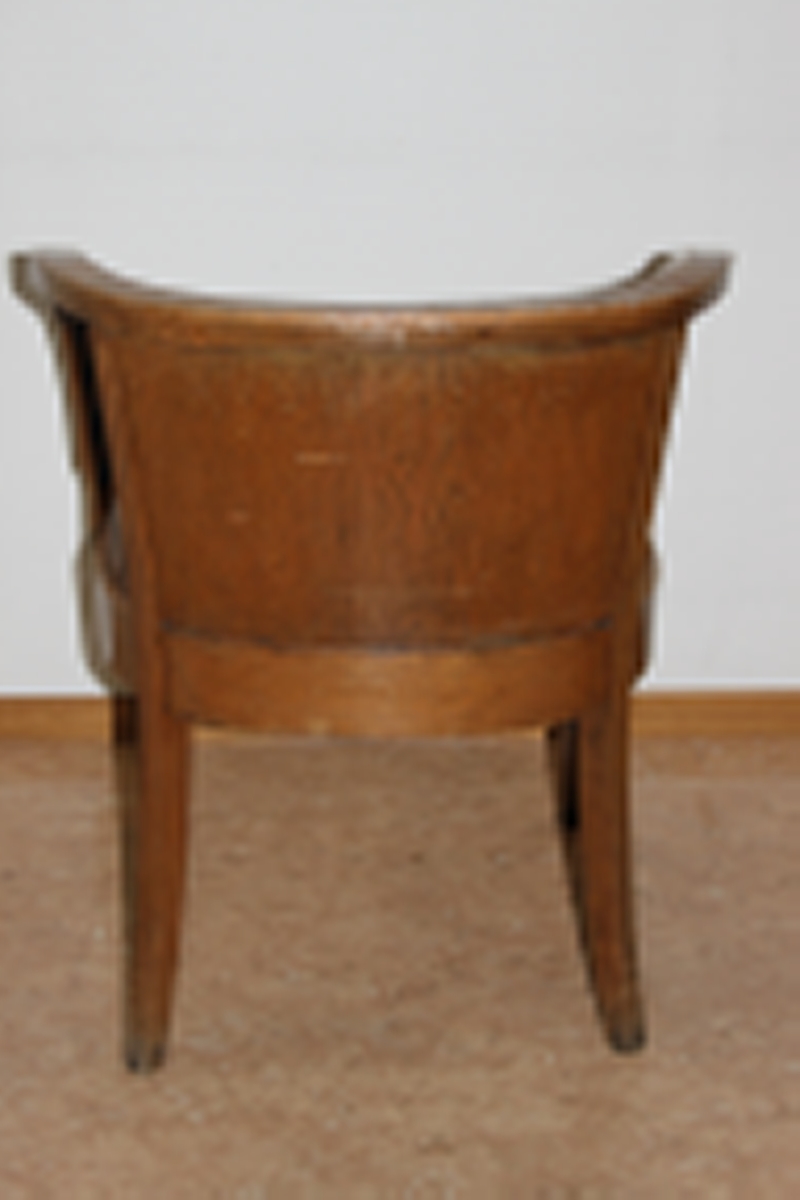 Møteromstol/kontorstol med armlener samt buet rygg. 4 ben. Metallbeslag under armlener. Brunt skinn i rygg og sete. Stolen er lakket med klar lakk. Originalt møbel innkjøpt til det nye Statsarkivet i Kristiansand i 1935.