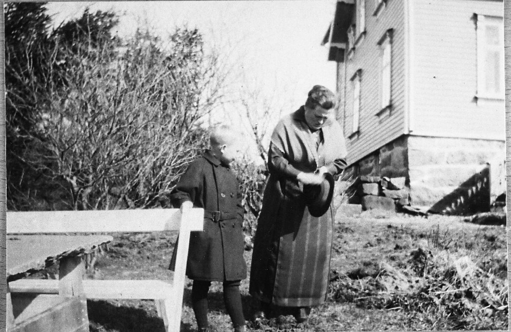 Odd Schibevaag (9.4.1912 - ) og mora Ellen Schibevaag f. Mossige 1.9.1881 - 14.2.1956) i hagen på Rossaland bnr. 20. Ser ut som ho finpussar hatten.