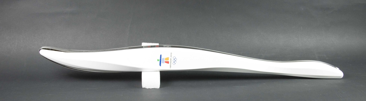 Hvit håndfakkel av plast og metall. Fakkelen har emblemet for de olympiske vinterleker i Vancouver i 2010. Det er også motiv av lønneblad på fakkelen.
