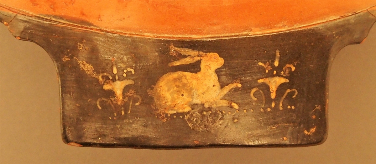 I skålens bunn naken mann (Dionysos) og kvinne med tamburin (mænade). Under dem en eggstav (kymation). Motivet er omgitt av løpende hund i sirkelform. På hankene hare og fugl. På undersiden palmettfrise (anthemion),løpende hund, mænade med tamburin og tromme og naken mann med olivengren (Apollon).