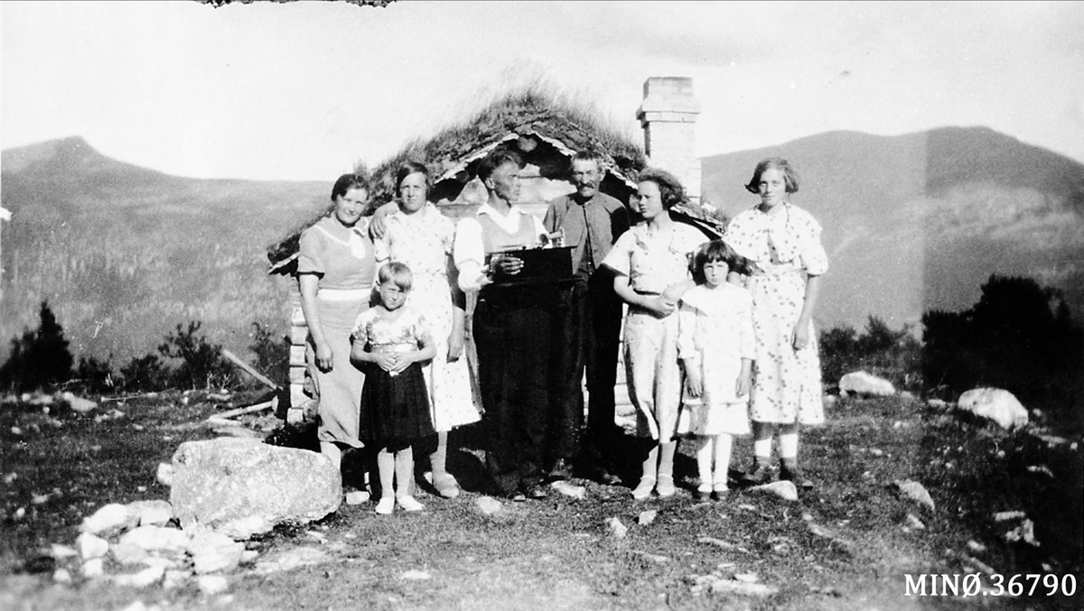 Personer oppstilt foran lita hytte