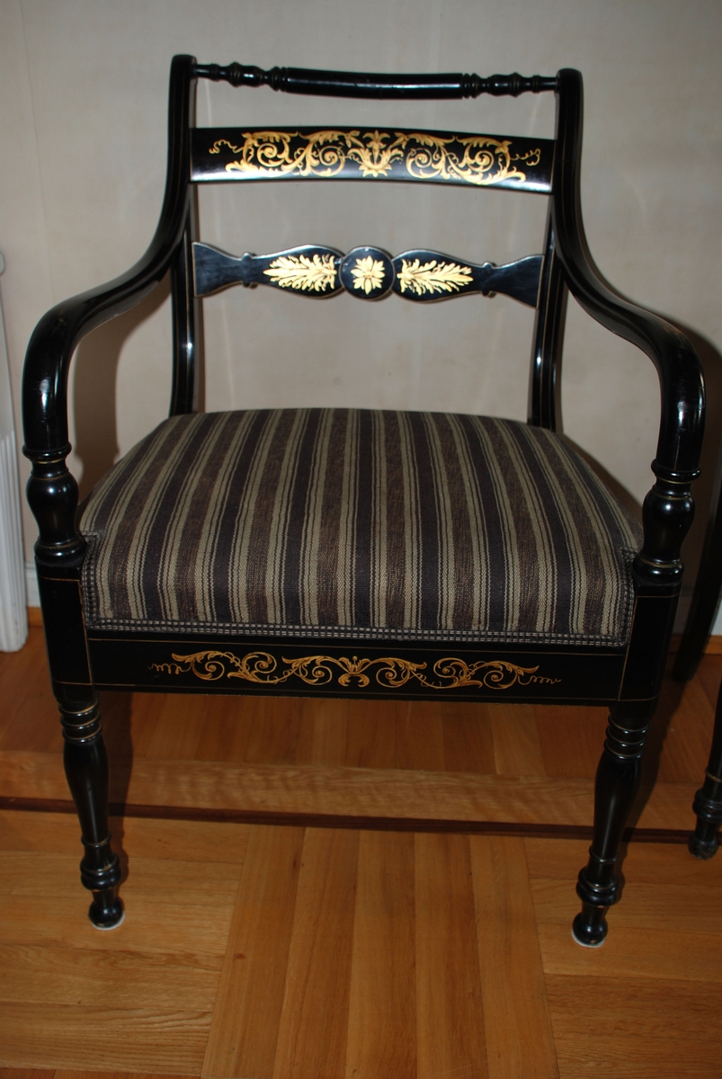 Svart stol laget av snekkerfirma Knag i Bergen. Tre ryggsprosser hvorav de to nederste har gulldekor. Gullpalmetter. Armelenene er s-svingede og ender i de dreiede frembenene. Gulldekor på fremsargen. Setet er trekt.