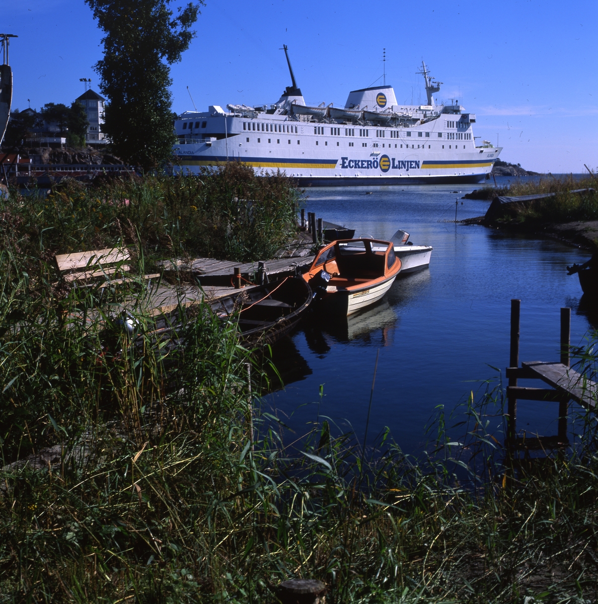 Fogdö, en ö i norra Roslagen, 2-3 september 1999.  Här ser vi färjan, några båtar vid en brygga och byggnader i bakgrunden.