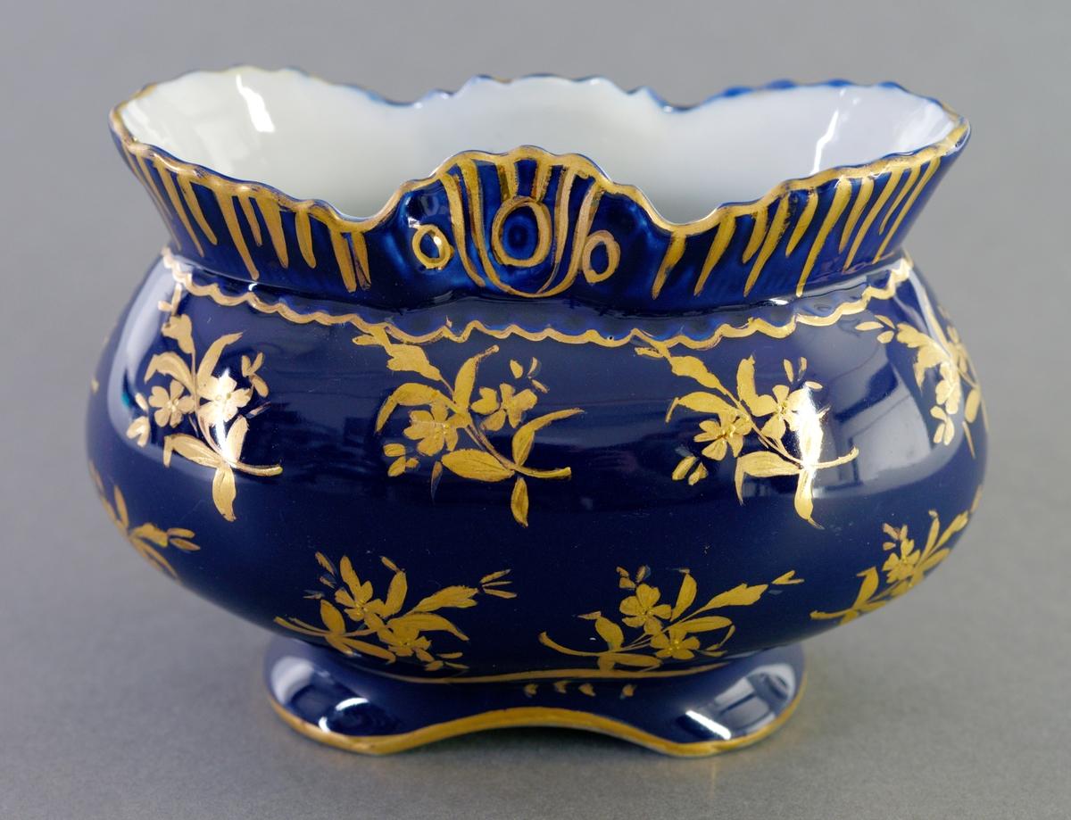 Oval skål av porselen med hvit glasur og blå farge. Håndmalt gulldekorasjoner av blomster og linjer.
Kan ha blitt brukt som pyntegjenstand.