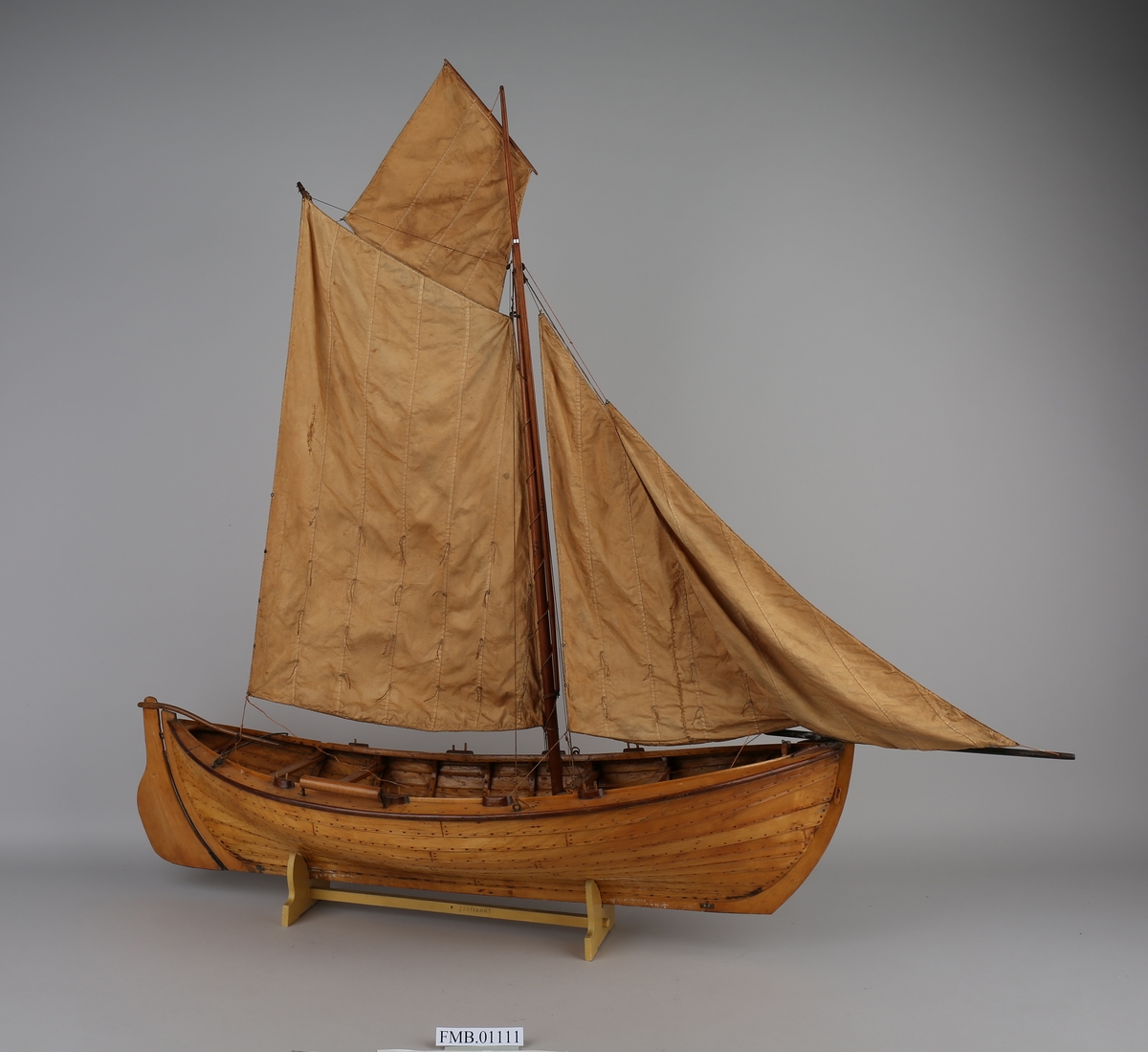 Modell av spririgget listerbåt med 2 rombeformede og 2 trekantede seil. På den ene båtripen er det festet en rull. Båten har 3 par årer.