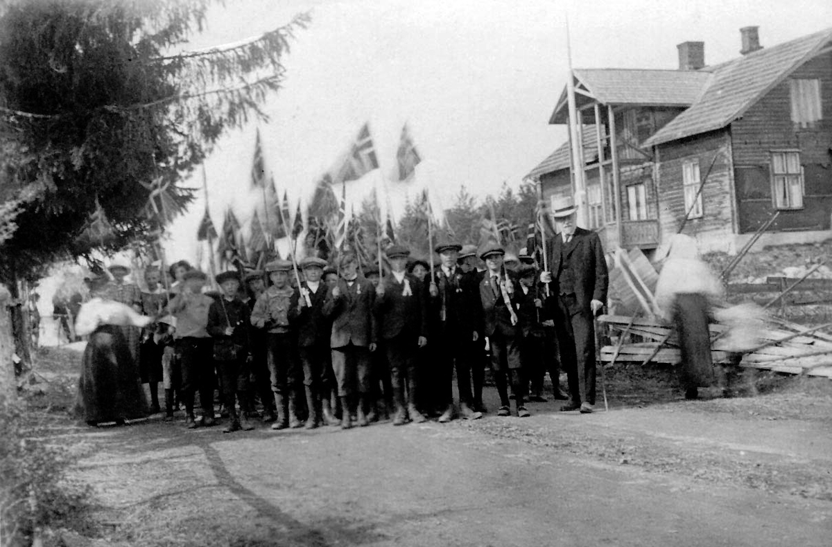 17-maitoget 1906 i vegen ved Løkken i Austvatn. Til høyre huset til baker Sandberg. Læreren i hatt er Reinhard Larsen.