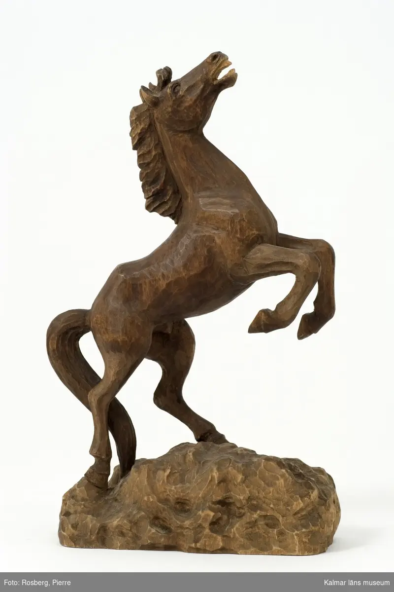 KLM 43830:2 Skulptur, av trä. Benämnd, Stegrande häst. Datering, 1960-talet. Signatur, HR. Figuren består av en häst som stegrar sig på berget.