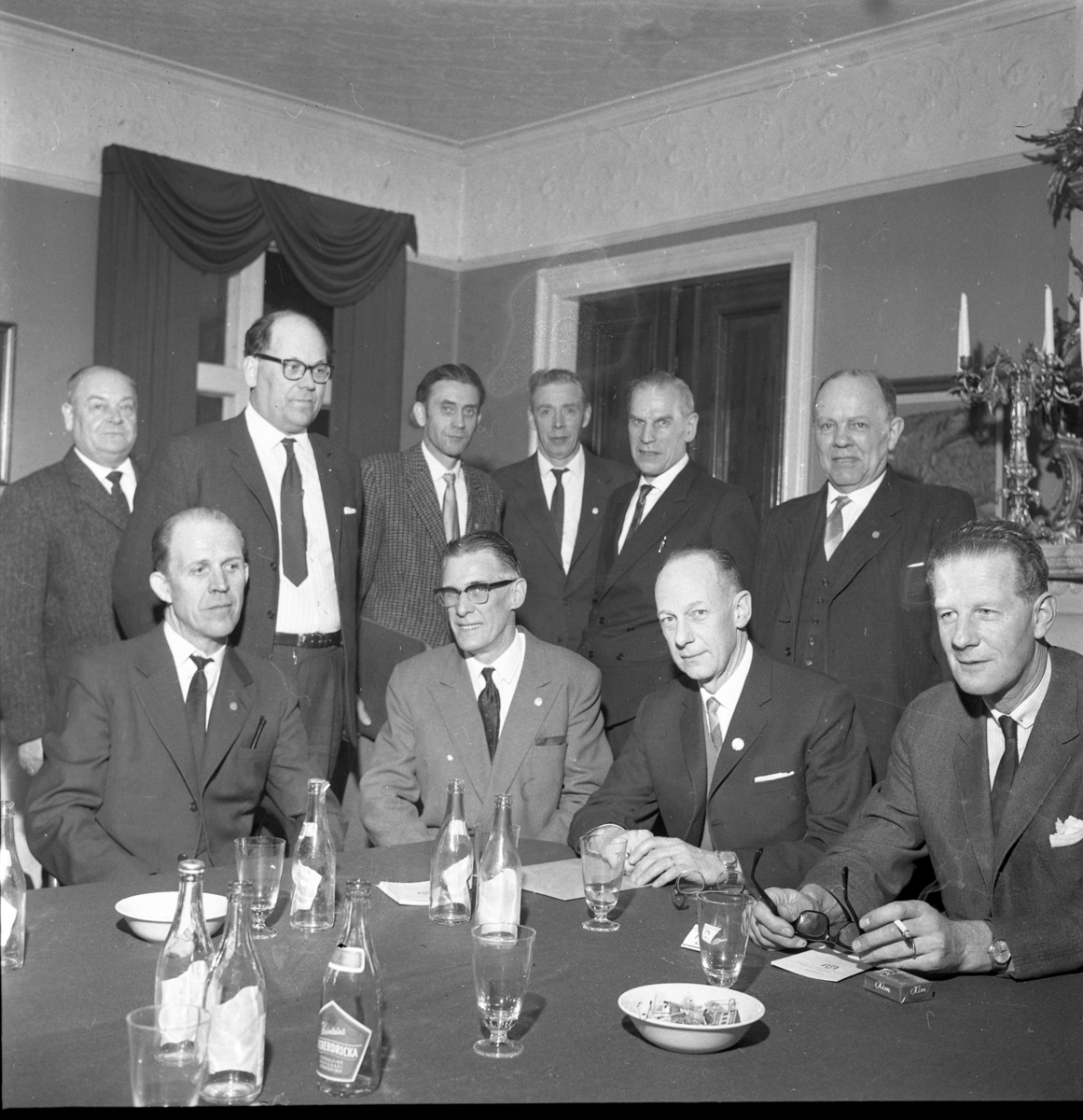 Målarmästarnas förening i Stockholm håller möte på Grand Hotel Ribbagården. Okända män sitter och står vid ett bord med askkopp, glas och tomma läskedrycksflaskor.