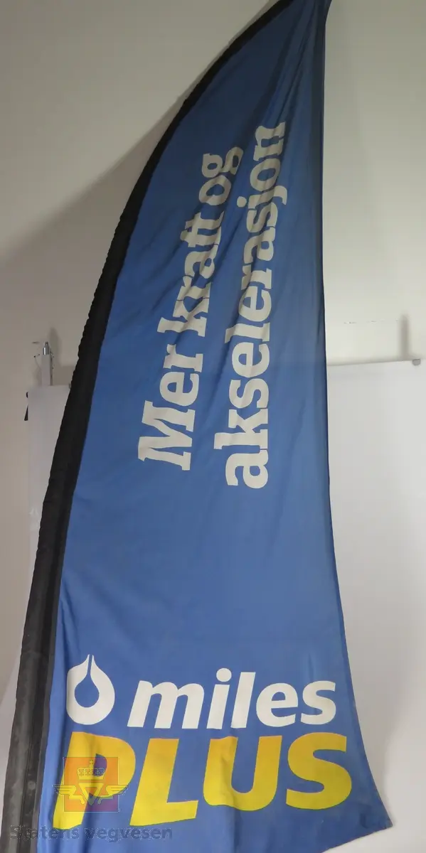 Flerfarget seil (banner) som er tredd inn på en buet metallstang. Stanga festes til en sokkel av plast. Denne kan fylles med vann for å stå stabilt.
