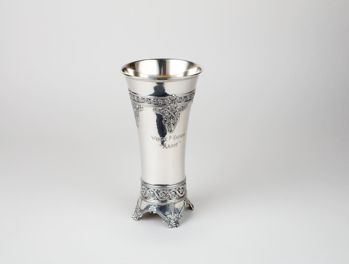 Pokal, sølv. Form som et middelalderbeger, dragestilsornamentikk. Stemplet på utsiden av et av bena.