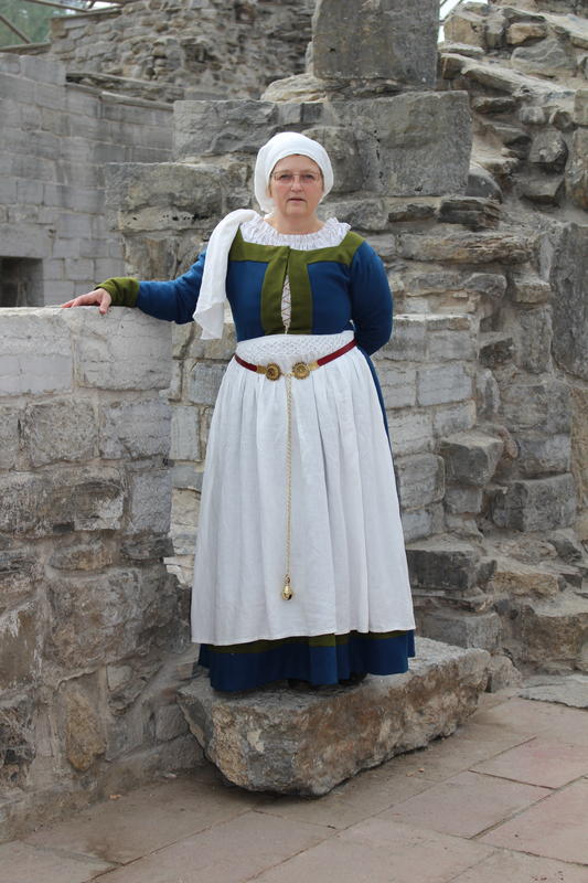 Kvinne i middelalderdrakt står og holder på en middelalderruin.