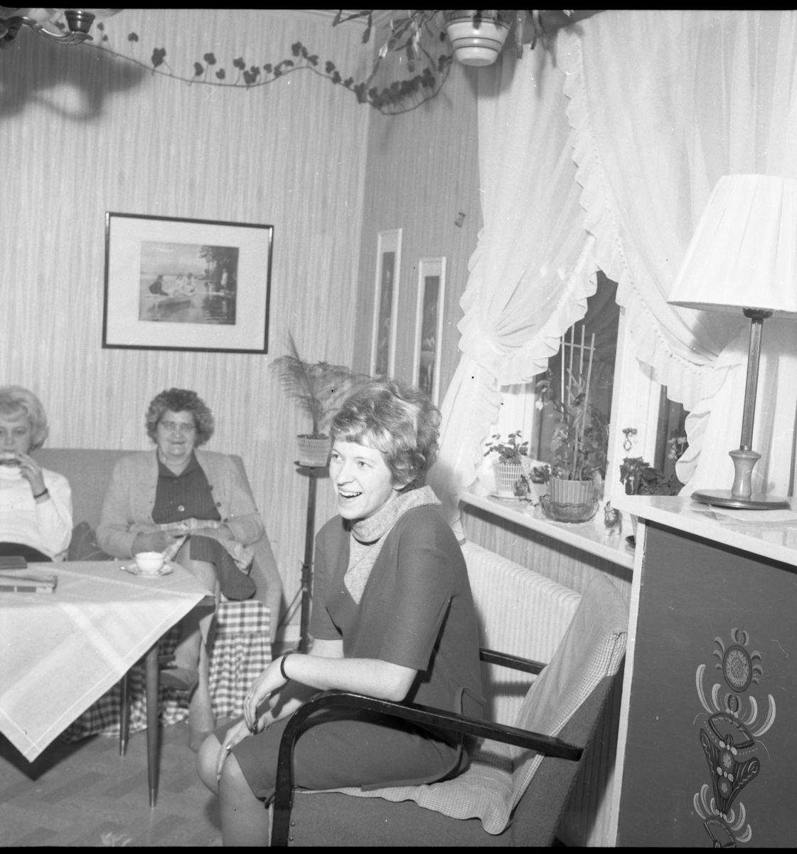 Interiör från ett hem. I soffan sitter Ulla Lago och Birgitta Blomqvist med kaffekopp på bordet. I fåtöljen sitter Gerd Lago.