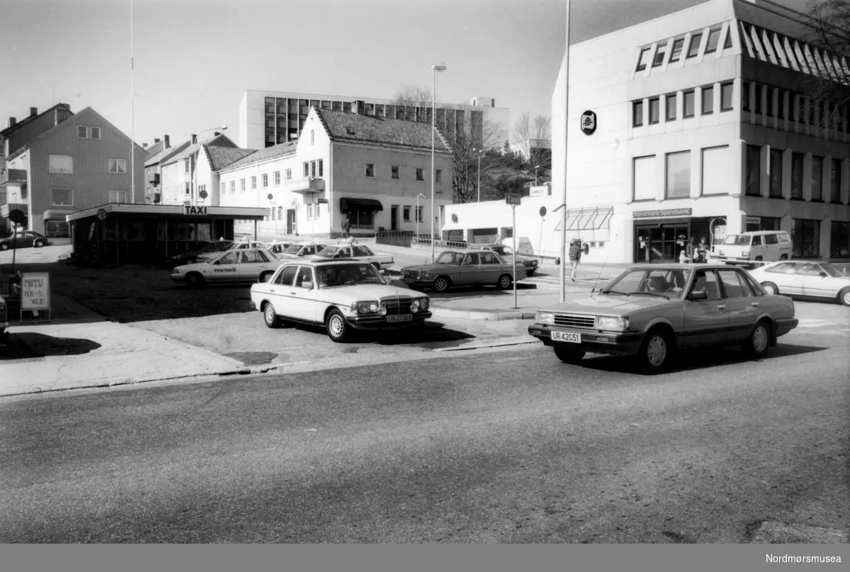 Pressefoto fra Langveien på Kirkelandet i Kristiansund, men Taxisentralen til venstre og Nordmøre Sparebank til høyre. Fotoarkivet stammer fra Nordmørsposten, og inngår nå i Nordmøre museums fotosamlinger.