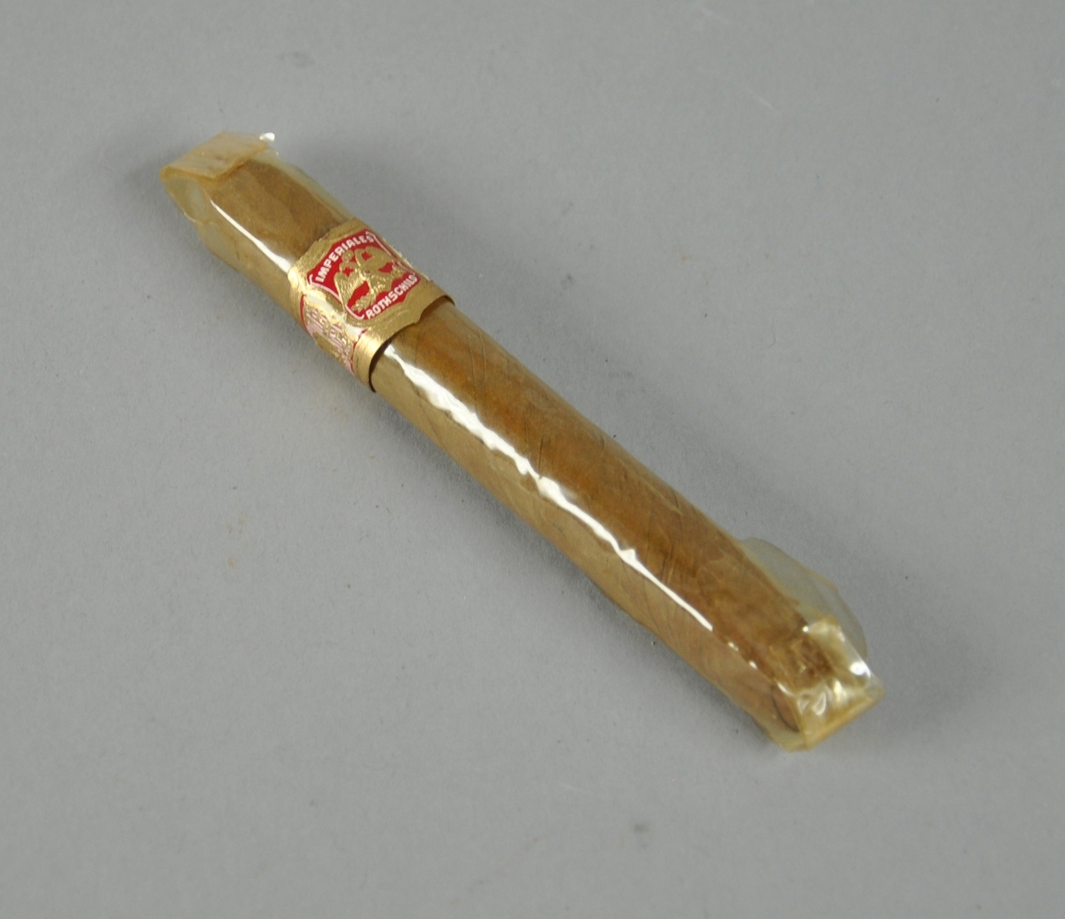 Sigaren er innpakket i cellofan med forseglede ender. Rundt sigaren gull-, rød- og hvitfarget mavebelte på utsiden av cellofanpakningen.