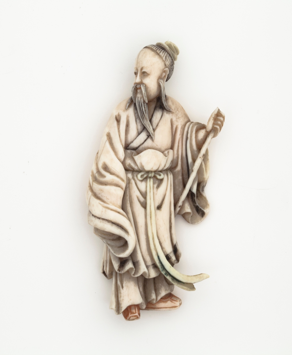 En elfenbensfigur av en eldre mann ikledd romslige gevanter. Han holder i en stokk. Figuren kan forestille en boklærd, en vismann eller en hellig mann. Ikonografien minner om lignende taoistiske representasjoner under Qingdynastiet.