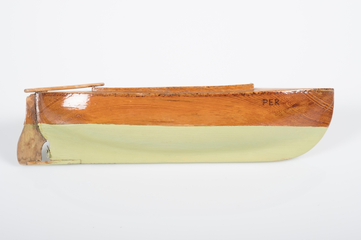 Liten lekebåt i tre/ modell av sørlandssnekke med ror og en liten propoell. Båten er lakkert grønn under vannlinjen og navnet "Per" er brent inn på begge sider.