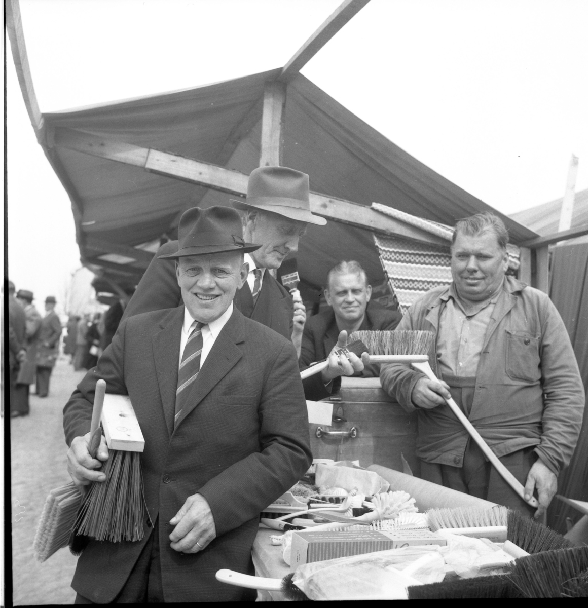 Marknad på Gränna torg. Borsthandlare Olle "Blindolle" Bunnstrand säljer borstar av olika slag till kostymklädda herrar med slips och hatt. Andra fr v är Axel Alin