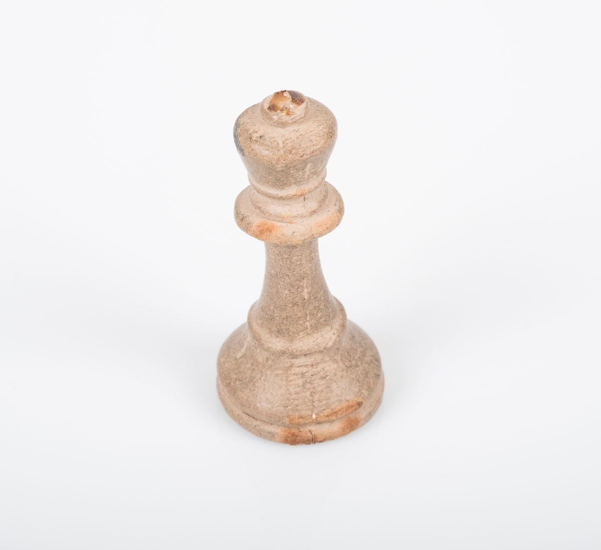 Sjakkbrikken (dronning) er laget av tre, og er malt hvit/grå. Det ser ut som den har blitt grå ved bruk. Lim på toppen av krona som tyder på at det har vært festet noe der, trolig et kors. Et lite hull på undersiden som er fylt med noe rosa.