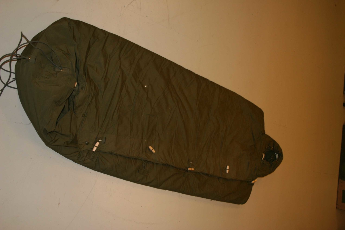 Soveposen består av yttertrekk og innertrekk med et mellomlag av kapokstoff. Disse deler er sammenknappet.
Overside av soveposen lukkes med knapping

