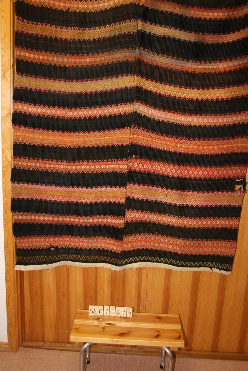 Rektangulært teppe med mønster, sydd saman av 2 breidder, falda og påsydd kanting i båe endar.