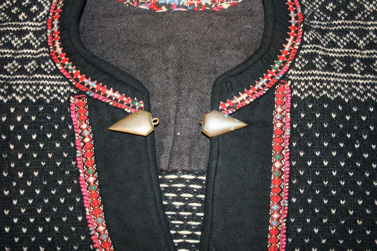 Strikka genser med kanting av svart klede rundt halsen og framme på ermane, broderi. 