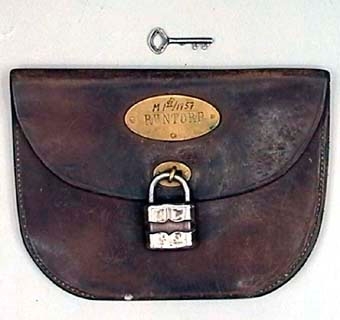 Remisspåse i väskform, halvmåneformad och av mörkbrunt läder. Med oval mässingsskylt med texten "Runtorp" samt låsanordning med litet förkromat hänglås. Med tillhörande nyckel.