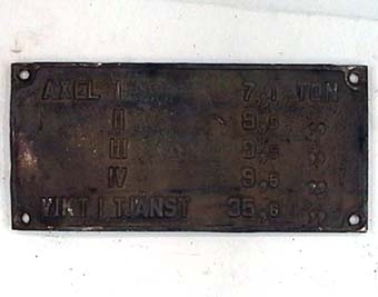 Rektangulär skylt av svart, förnicklad mässing, med text i relief.
Text på skylt: 

AXEL I 7,1 TON
II 9,5 "
III 9,5 "
IV 9,5 "
VIKT I TJÄNST 35,6 "