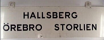 Rektangulär dubbelsidig plåtskylt med svart text på vit botten:
"Hallsberg - Örebro - Storlien",
Samma text på andra sidan.