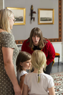 En omviser i kostyme snakker til to barn i Eidsvollsbygningen