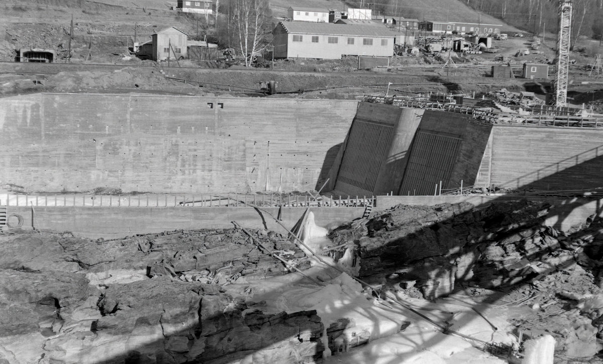 Anleggsområde i forbindelse med bygginga av et kraftverk ved Harpefoss i Gudbransdalslågen.  Dette fotografiet er tatt ved dem som skulle bli «dammen» kraftverksmagasinet med høye murer av armert betong.  Denne dammen ligger ved garden Solbrå, like nord for det trange elvegjelet med fossefall som her ble regulert til fordel for samfunnets energibehov.  Kraftverket utnytter et fall på 34 meter i Gudbrandsdalslågen.  Det ble satt i drift i 1965.  Kraftstasjonen ved Harpefossen har to kaplanturbiner og en årsproduksjon på 427 GWh.
