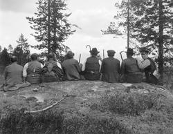 Gruppe med åtte menn, fotografert sittende på en rund bergna