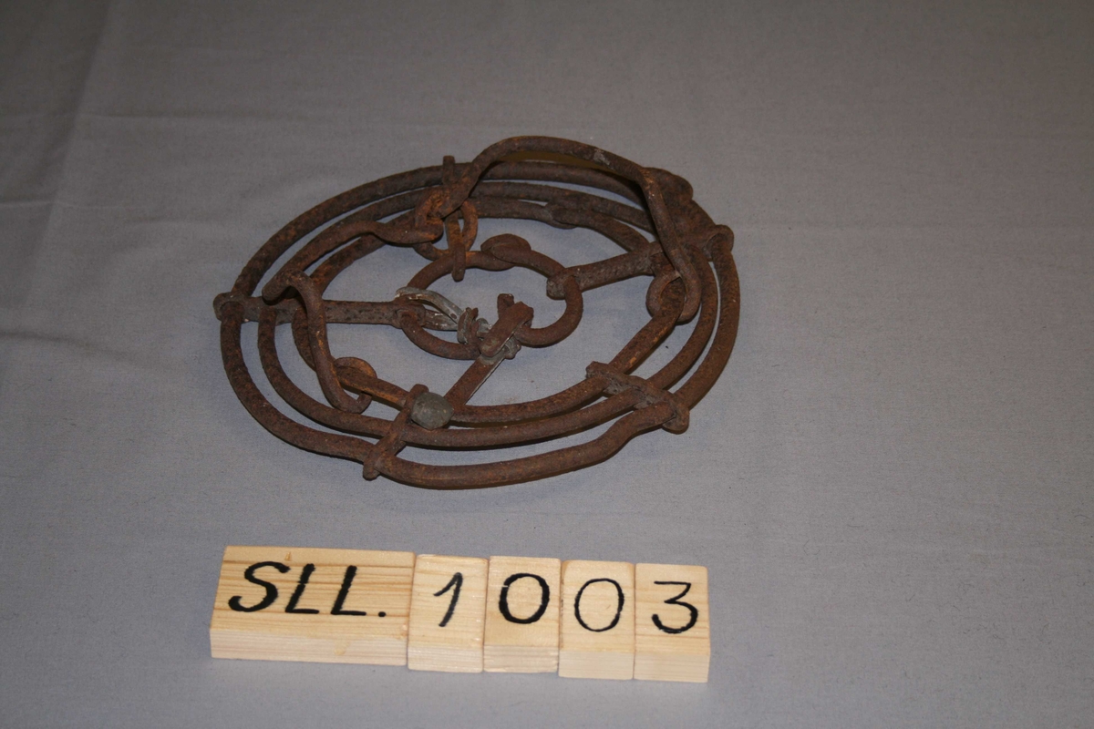 Tilnærma sirkulær, laga av jern. 4 ringar, bundne saman med jernstag, 2 bøyelar til å feste på hoven. reparert med tykk jerntråd og ein stor spiker.