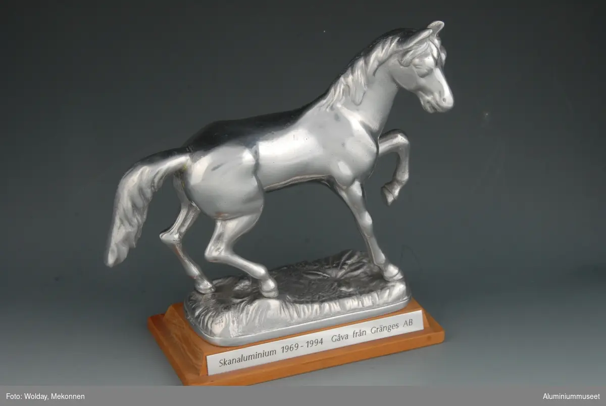 Hesteskulptur plassert på en fot. Foten har en plakett med inskripsjon
Hesten står i en aktiv posisjon med venstre forben høyt hevet, hodet løftet og vendt mot høyre.