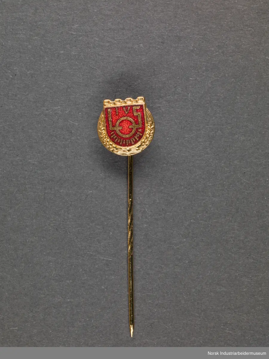 Gullfarget jakkenål. Motivet er "LOS IV" skrevet i gull på rød bakgrunn. Bladkrans og krone.