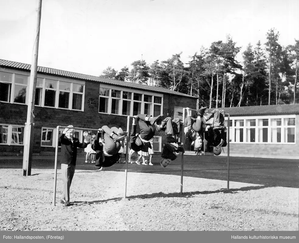 Invigning av Bläshammars skola. I förgrunden leker pojkar i klätterställning. På skolgården står en grupp flickor i uniform.