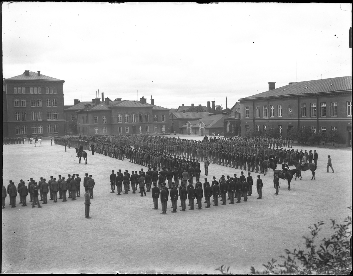 Uniformerade militärer uppställda på gårdsplan utanför garnisonsbyggnaden. Bilden tagen under fotografen Harald Olssons excercistid.