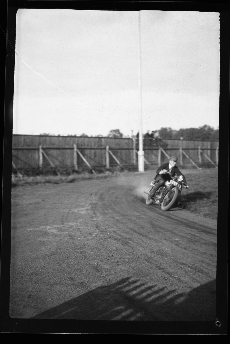 En man kör motorcykel på en grusad bana. I fotografens anteckningar står det: "2 film från Motorcykellopp (Idrottsp.)".