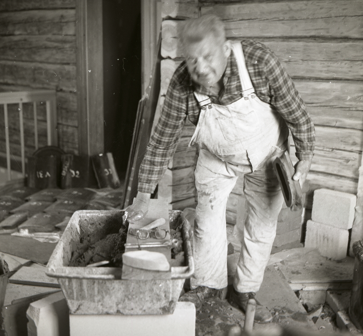 En man tillverkar murbruk för att sätta upp en kakelugn, 1968.