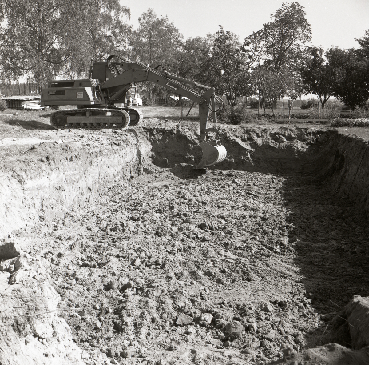 En grävmaskin gräver ett fyrkantigt hål i förberedelse för en husgrund i Glössbo, 1967.