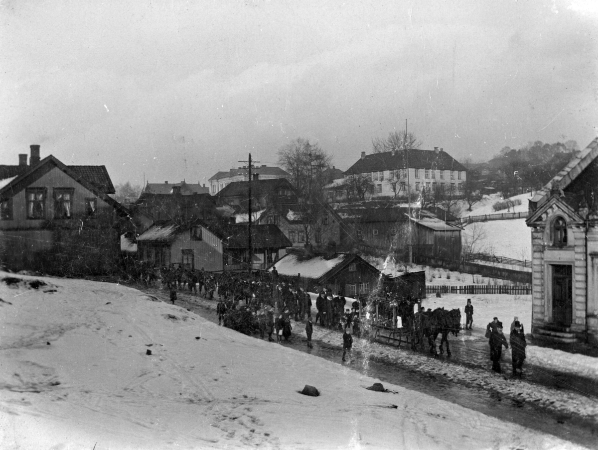 Begravelsesfølge med katafalk på meier, retning syd ned Kverndalsgate, Skien ant. før 1910.
Trebygg i bakgrunn, Wattenberggården og smie.