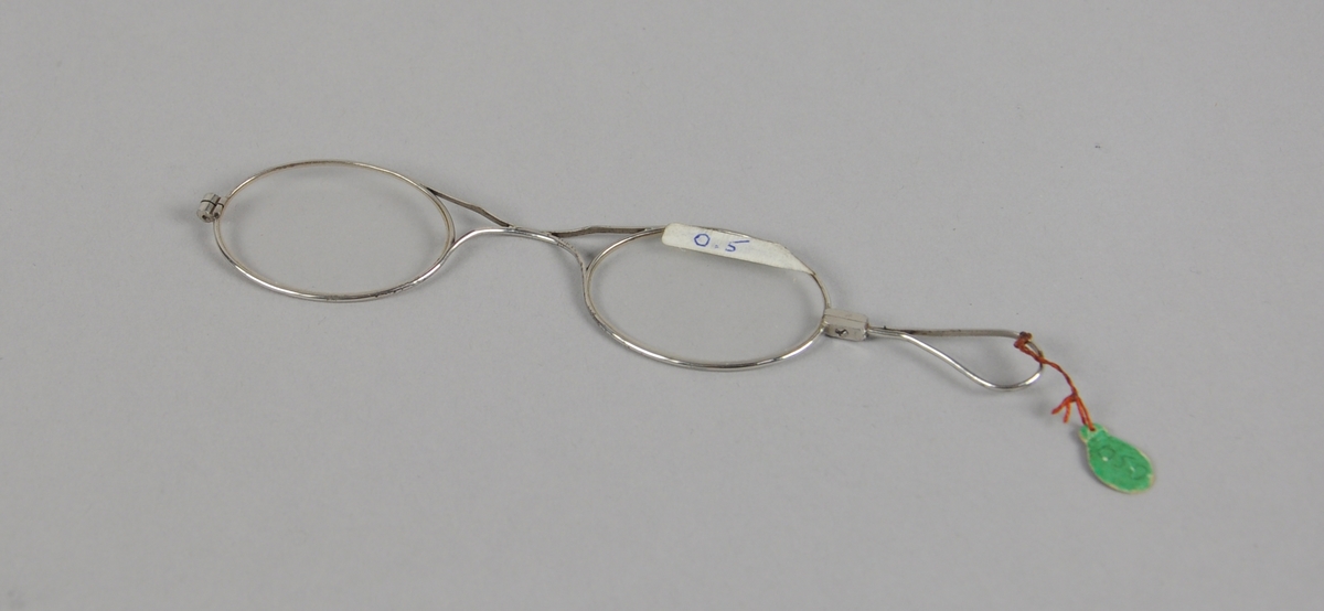 Ovale briller med metallinnfatning. Det er en hempe på den ene siden av brilleglassene.