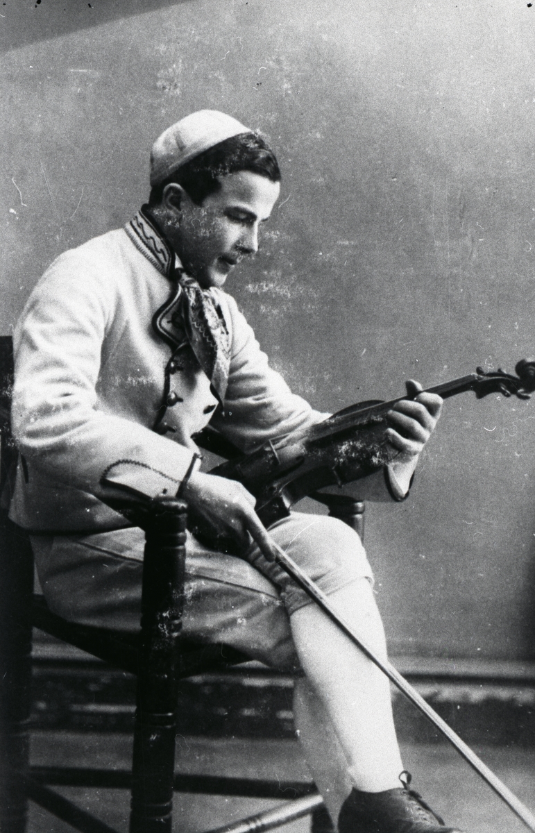 En man sitter på en stol och håller i en fiol.