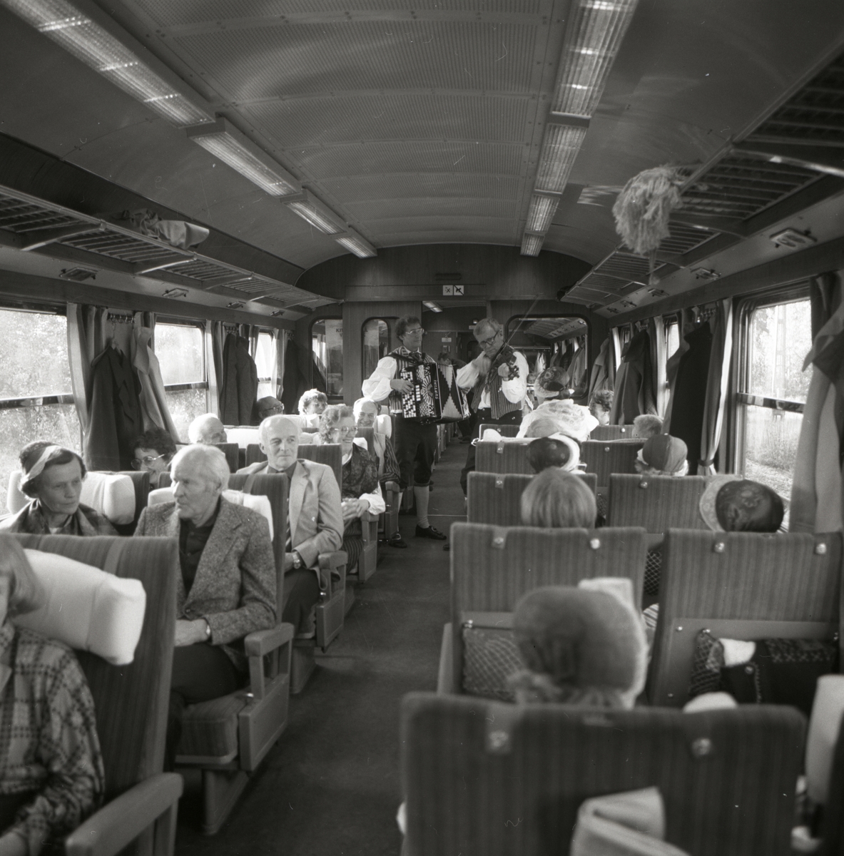 I en tågvagn står två spelmän med dragspel samt fiol och underhåller de resande, 1986.