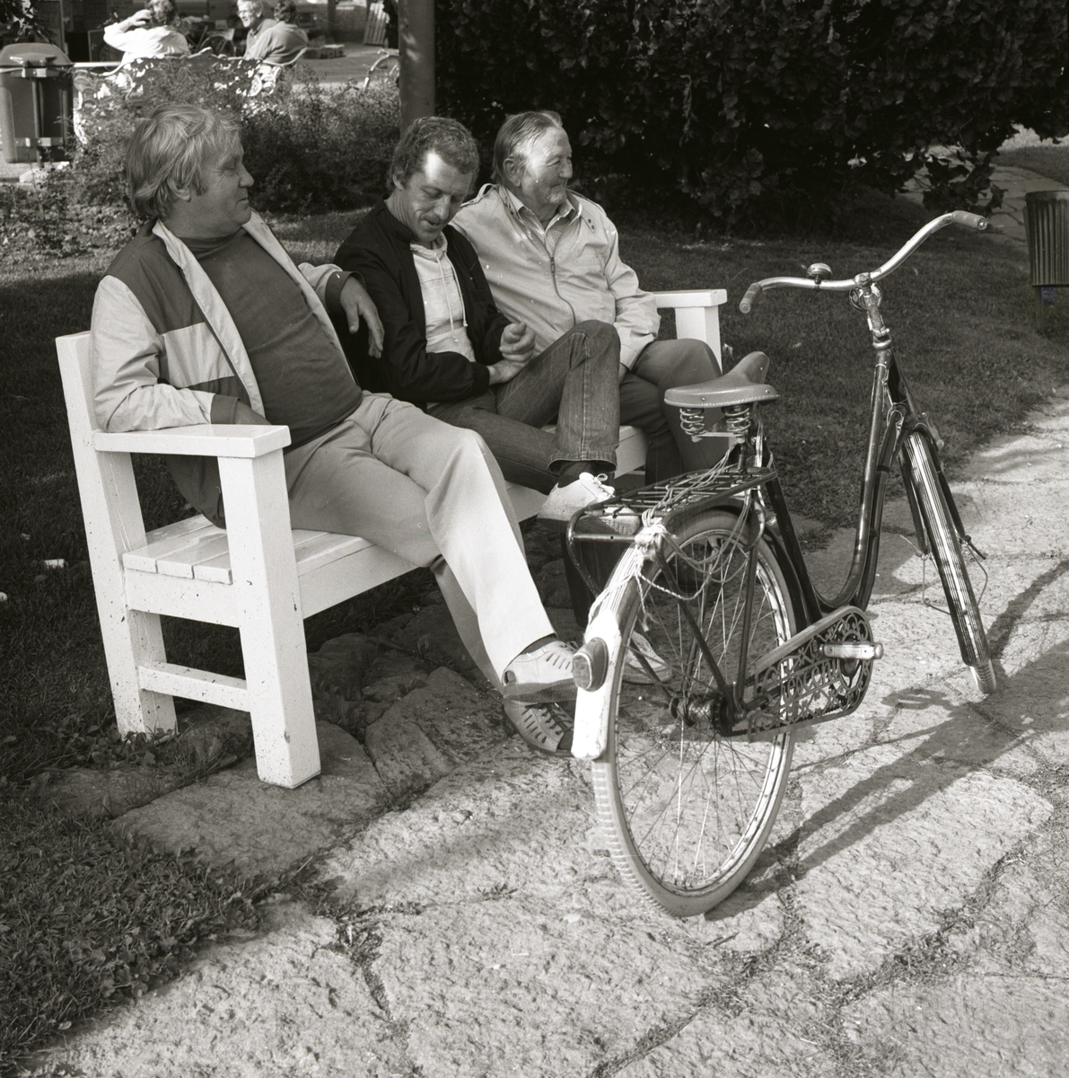 Tre män sitter på en bänk och framför dem står en cykel.