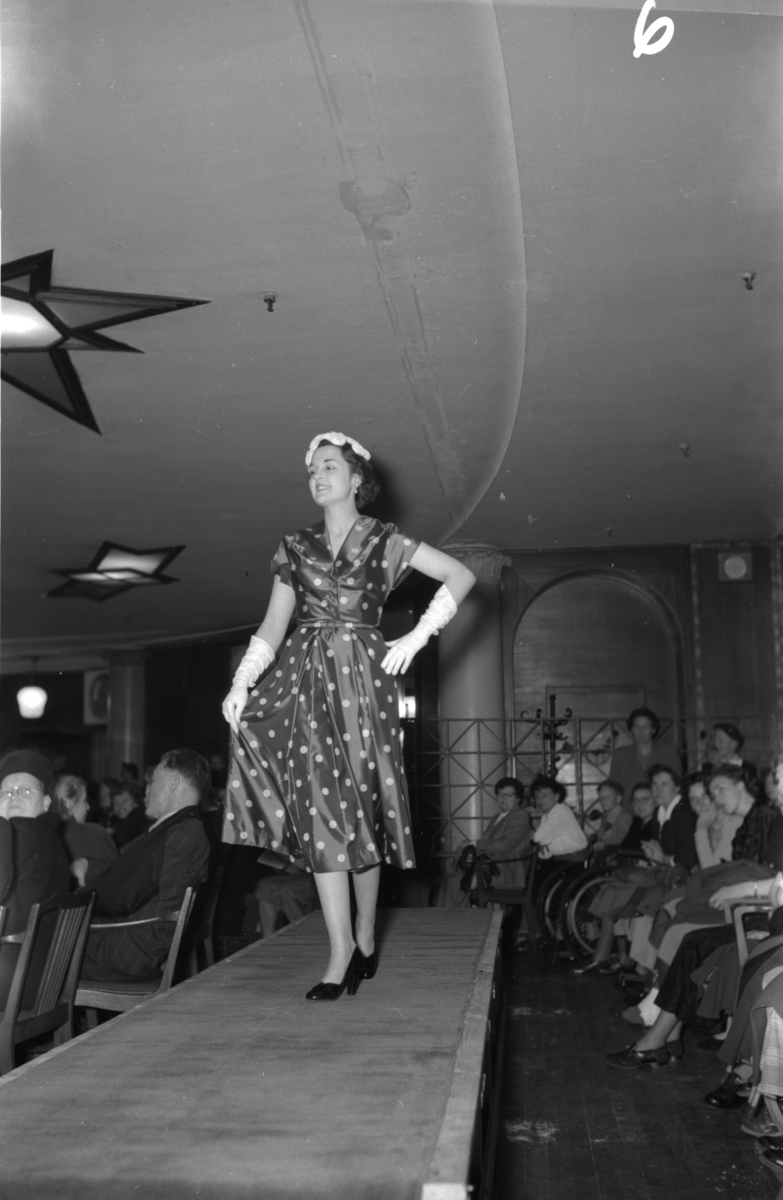 En kvinne på podiet iført prikkete kjole. Fra en motevisning på Steen & Strøm fra 7. mai 1954..