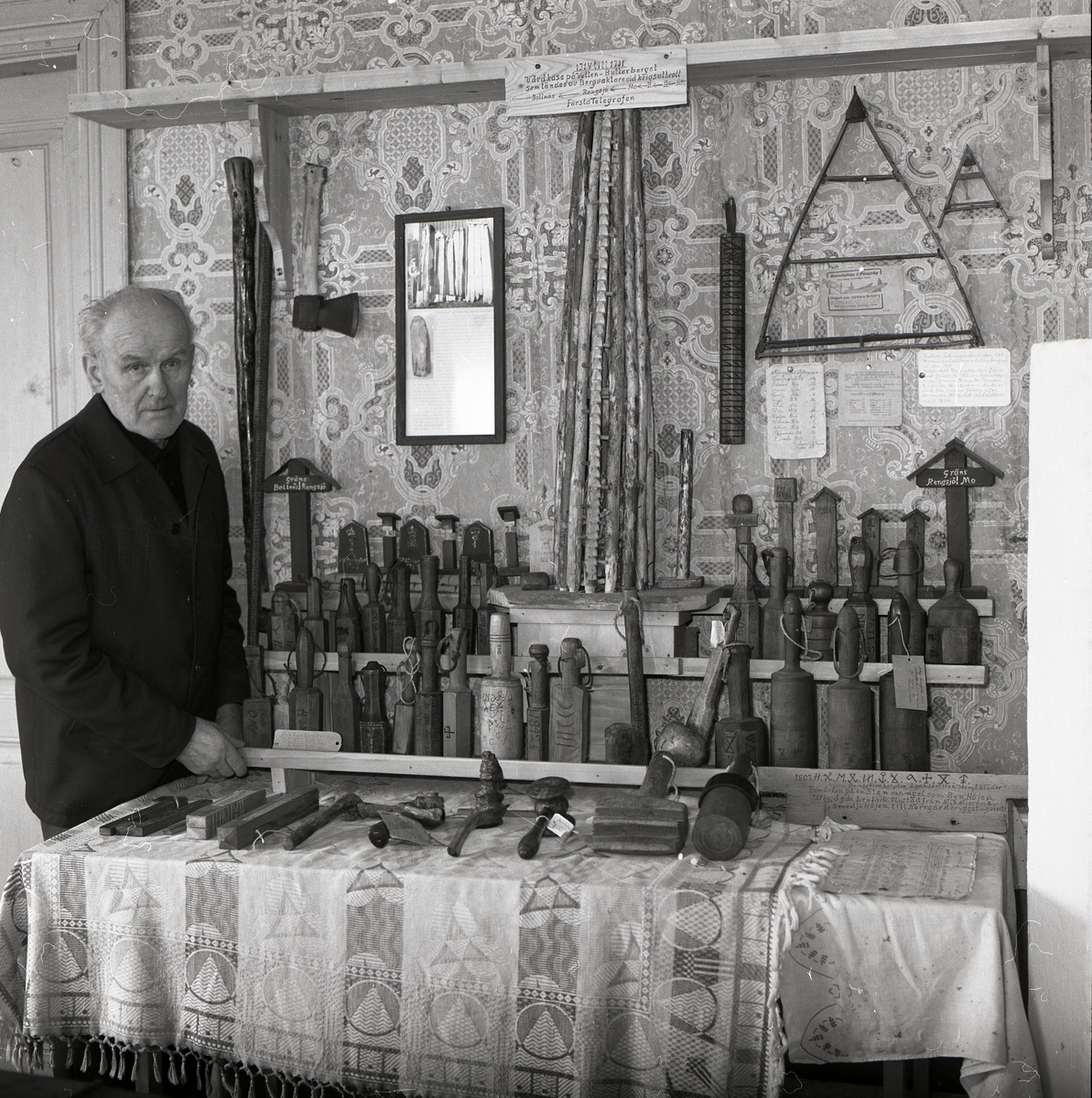 En man står i ett rum och tittar på en samling föremål som till största delen består av byklubbor, hösten 1982.