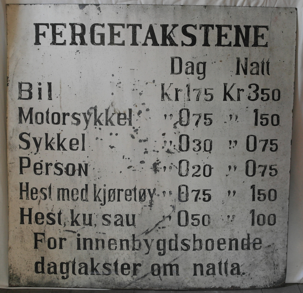 Skilt i blikk, malt med hvit bunn og svart tekst. 
Skiltet gir informasjon om ferjetakster og ble brukt til Skarpeid-ferja, trekkferje som gikk over Trysfjorden i Søgne frem til 1963.